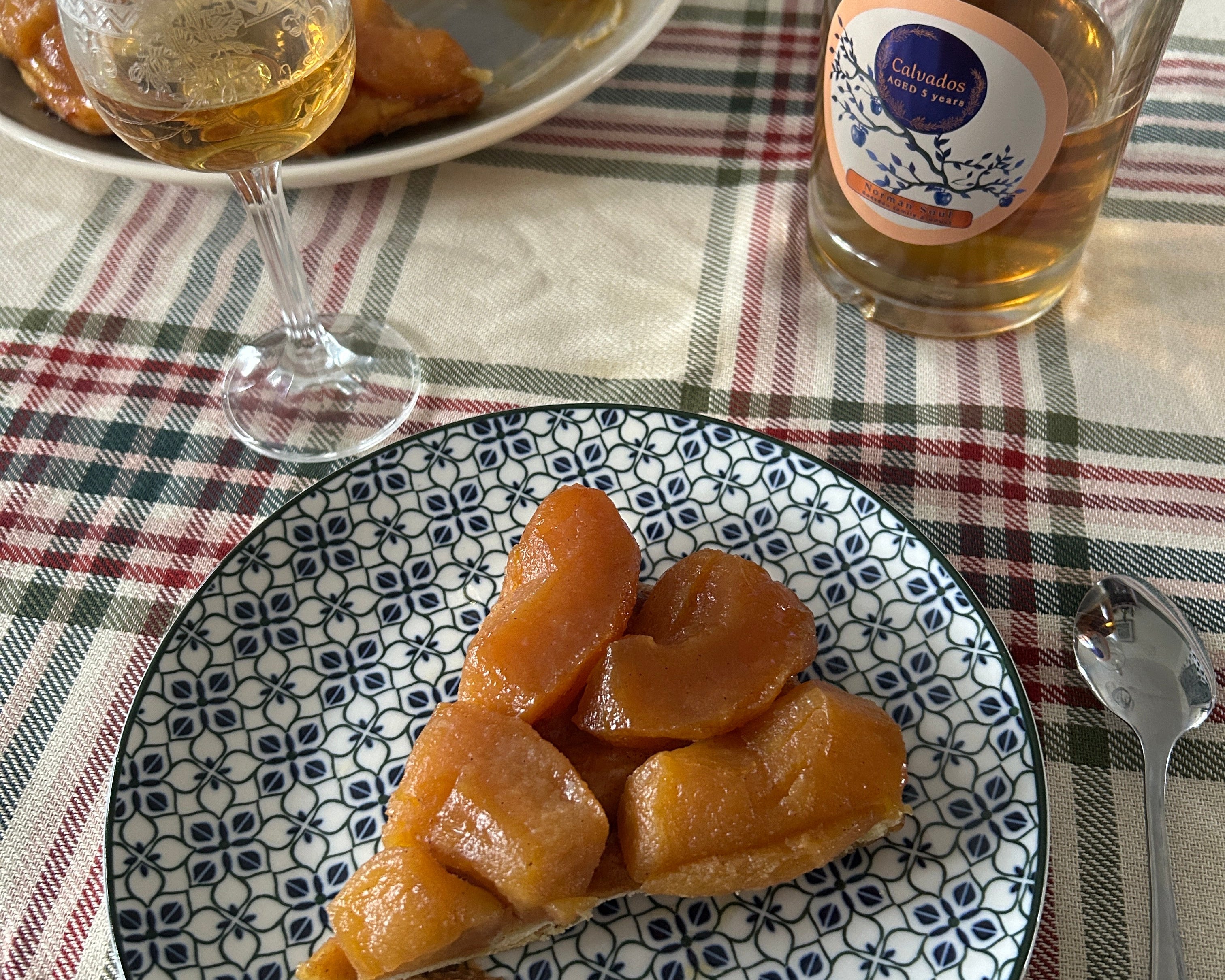 Tarte Tatin on a patterned plate with a glass of Calvados wine on a checkered tablecloth